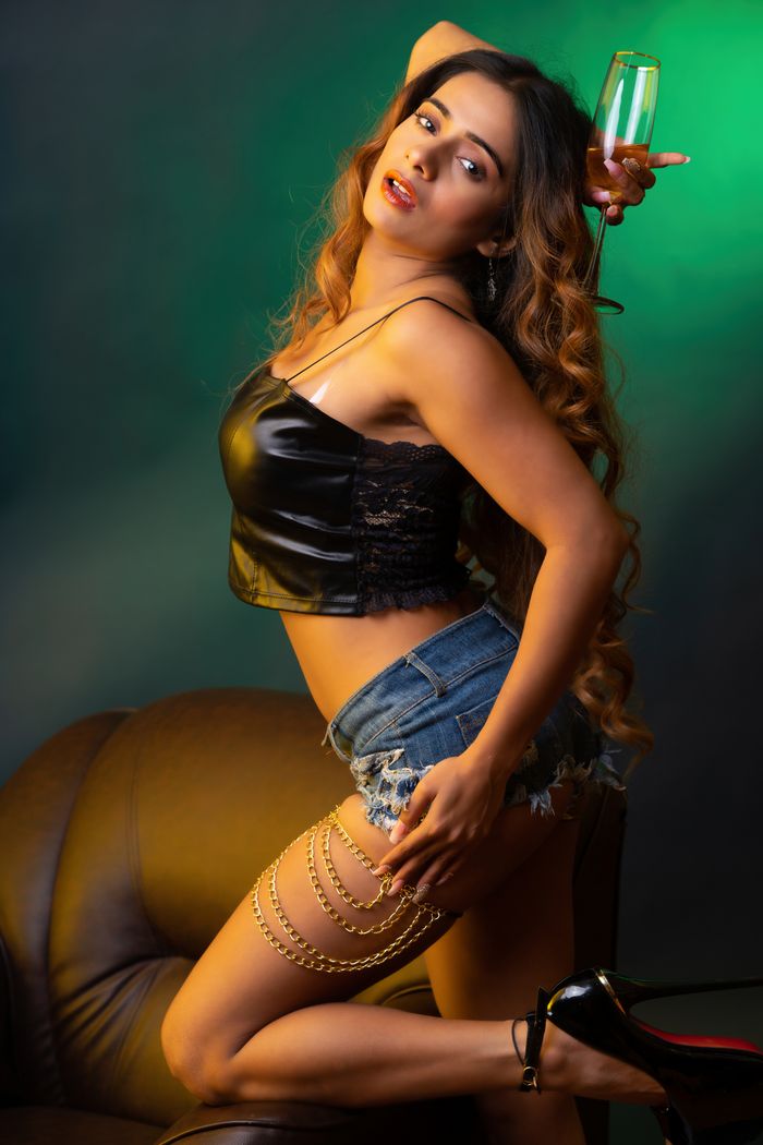 Elegant woman in a stylish outfit posing with a champagne glass on a studio set.